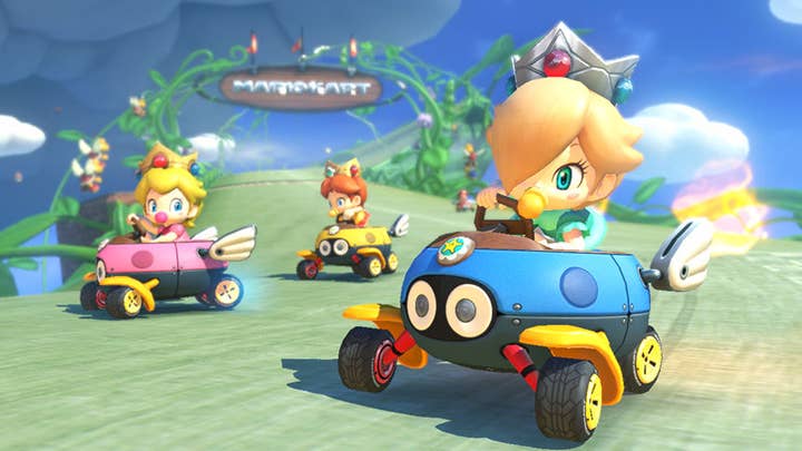 Baby Peach, Baby Daisy, and Baby Rosalina drive around an elevated track in a Mario Kart game