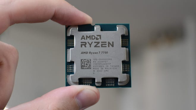 An AMD Ryzen 7 7700 CPU being held between a finger and thumb.