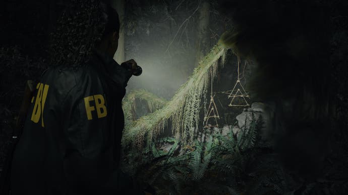 Alan Wake 2 screenshot showing Saga in left foreground pointiner her flashlight at some mossy overgrowth in the dark, closer now showing some hanging triangle shapes