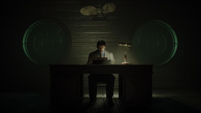 Alan Wake 2 screenshot showing Alan Wake sitting behind his desk facing the camera, writing on his typewriter with just a faint desk lamp on