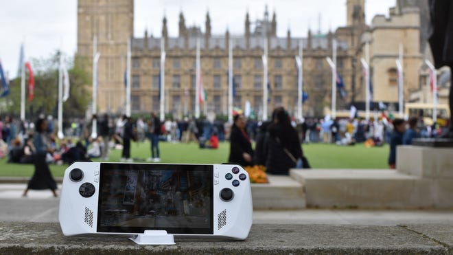 An Asus ROG Ally running Cyberpunk 2077, while sat on a wall near the Houses of Parliament.