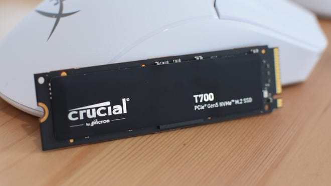The Crucial T700 SSD, without its heatsink, leaning against a gaming mouse.