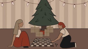 Two people play Chess together in front of a Christmas tree.