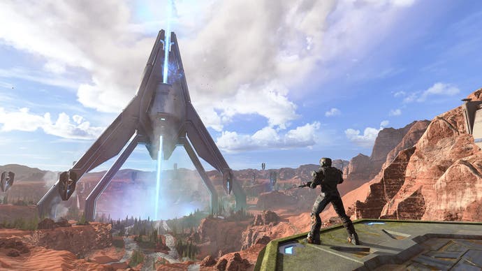 The Oasis map in Halo Infinite - a huge metal building fires light down into the ground as a player watches on.