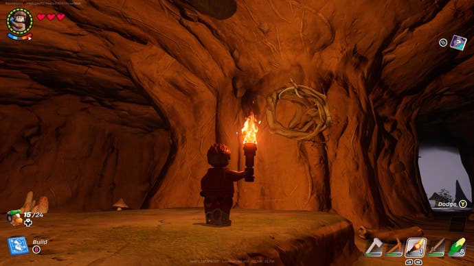 a lego character holding a lit torch looking at knotwood growing from a cave wall