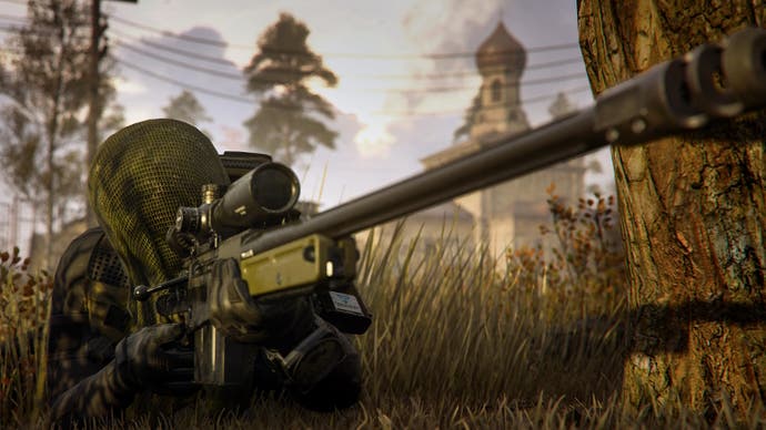 a soldier in a gilly suit prone in the grass beside a tree, using a sniper rifle