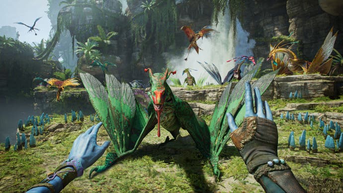 A screenshot from the new Avatar game. We see from the first-person perspective of a Na'vi, whose blue-skinned hands are held out in front of the player as they attempt to soothe and approach an Ikran, a large, flying lizard.