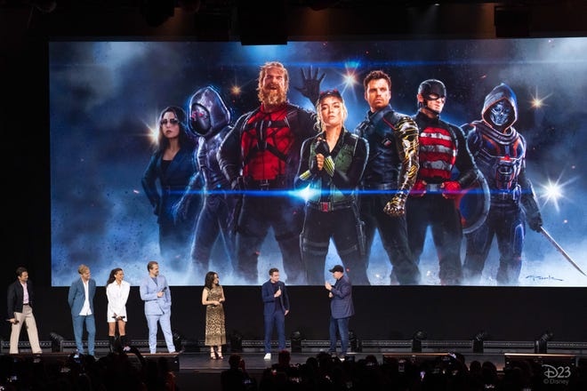 Photograph of the cast of Thunderbolts ons tage in front of an image of them in costume
