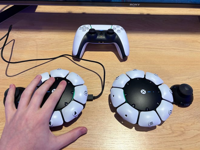 Photo of two Access controllers next to a DualSense, with a hand on the left hand side