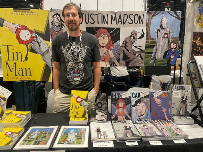 Image of Justin Madson standing behind his comics