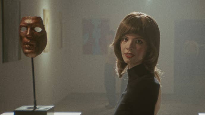 Karakter Franny dalam film Marissa Marcel kedua dari Immortality, Minsky, berdiri di samping topeng di sebuah pameran seni