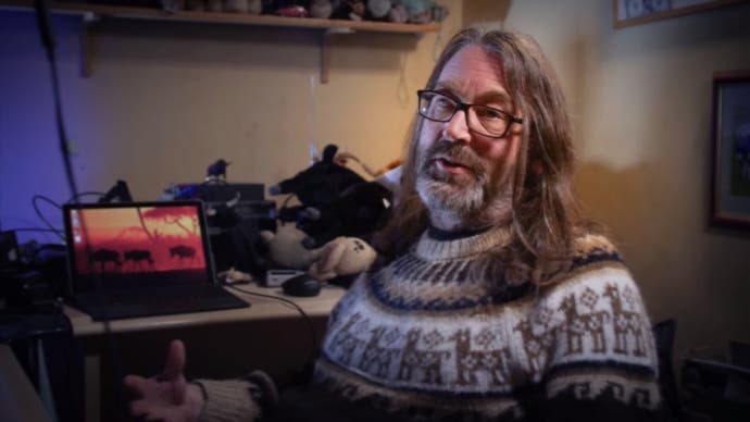 Jeff Minter wearing a sweater and talking to the camera in Llamasoft: The Jeff Minter Story.