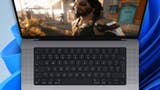 A Mac laptop shown, with Cyberpunk 2077 key art on the screen and the default Windows background behind the laptop.