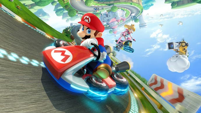 Mario driving his signature red kart in Mario Kart 8 with Peach jumping behind him and a Lakitu filming Mario