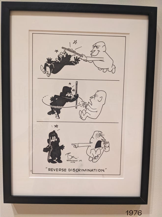 Photo of a Brumsic Brandon Jr. cartoon of a white figure hitting a black figure with a stick, the black figure turning in retaliation, and the white figure running away and pointing