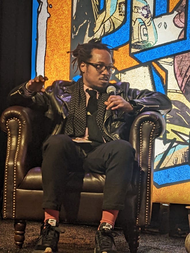 Photograph of Ronald Wimberly sitting on a leather chair and holding a microphone