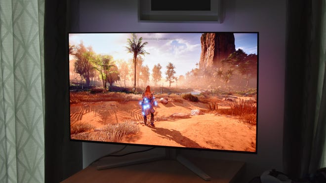 The Philips Evnia 42M2N8900 gaming monitor in a darkened room, showing its Ambiglow ambient lighting matching Horizon Zero Dawn on-screen.