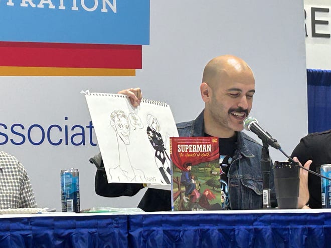 Writer and artist Sina Grace holds up sketches from the Superman: Harvests of Youth graphic novel.