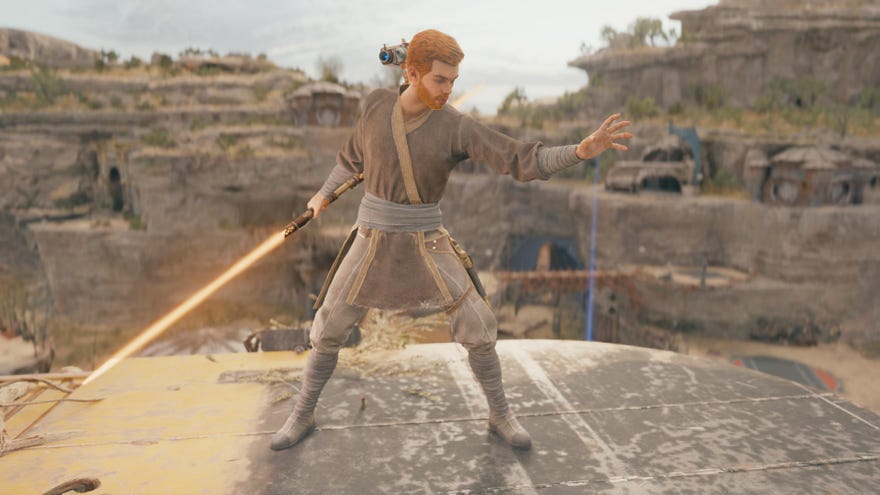 Star Wars Jedi Survivor screenshot showing Cal Kestis on a sandy ledge, wearing Jedi Robes and wielding an orange lightsaber in his right hand. His left hand is outstretched.