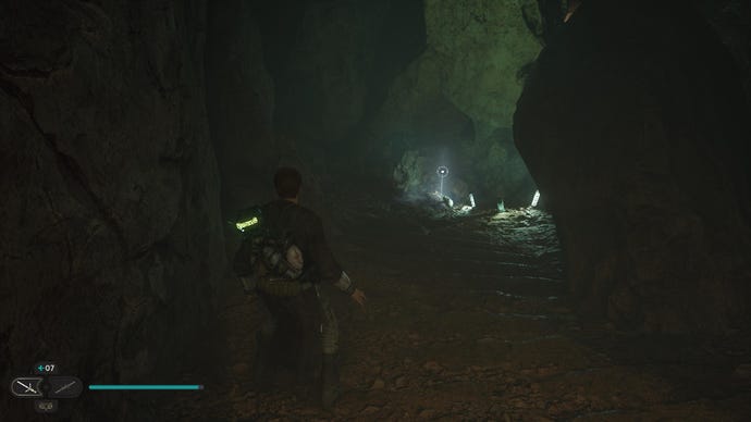 Star Wars Jedi: Survivor screenshot showing Cal stood in a dark tunnel, with a dim green glow up ahead.