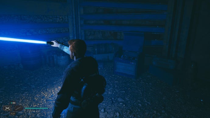 Star Wars Jedi Survivor screenshot showing Cal holding up a lightsaber to illuminate a chest in a dark cave.