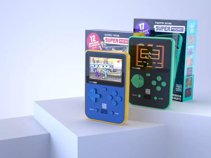 Two Super Pocket devices stand on a podium, with the boxes they're shipped in propped up behind them.