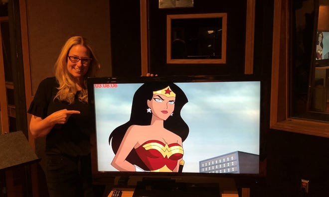 Voice actor Susan Eisenberg standing next to a TV with an image of Wonder Woman, a superhero, standing