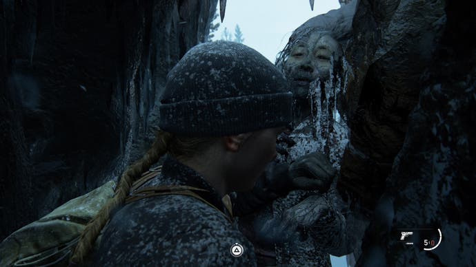 Abby pushes through a small opening in the rock and comes face to face with a frozen hiker. The triangle button is on screen as a button prompt.
