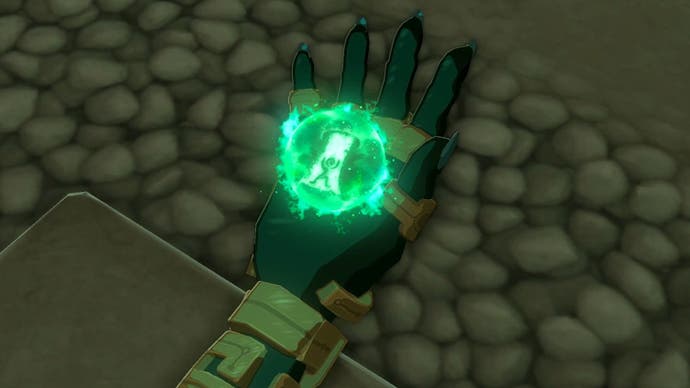 图片取自《塞尔达传说:王国之泪》，展示了林克的手拿着一个发光的绿色球体的特写，因为这个角色学会了提升能力。
