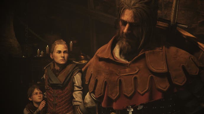 A close-up of Arno, a new soldier companion in A Plague Tale Requiem. He's got long greying hair tied in a top knot, and a scraggy beard. He's thick set, with a thick leather hood (that's down) around his shoulders, and big shield on his back. A young woman (Amicia) and young boy (Hugo) look up at him.