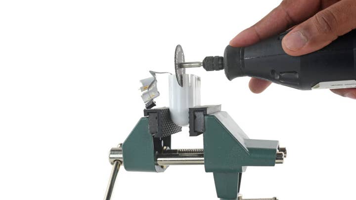 An AirPod charging case is held in a vise grip as a hand holding a Dremel tool cuts into it in an attempt to access the case interior