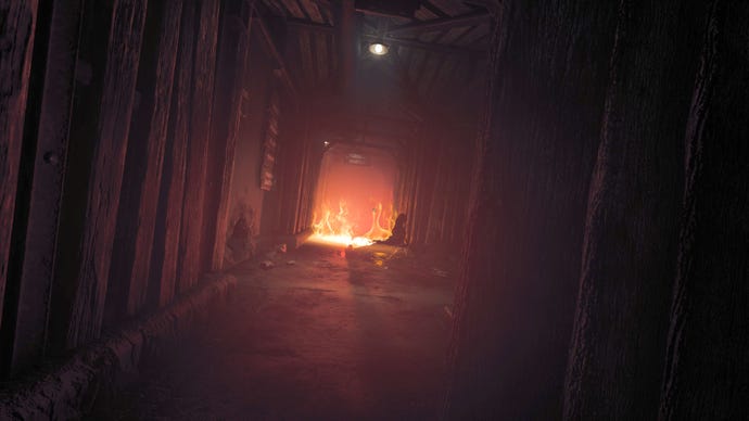 Leaning to look down a dark hallway in Amnesia: The Bunker, with a fire silhouetting a dead body at the other end