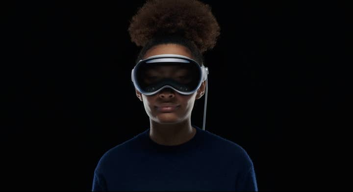 A woman wearing the Apple Vision Pro headset and looking straight at the camera. You can see her eyes dimly through the semi-transparent visor