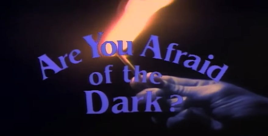 Hand holding a lit match behind the words Are you Afraid of the Dark?