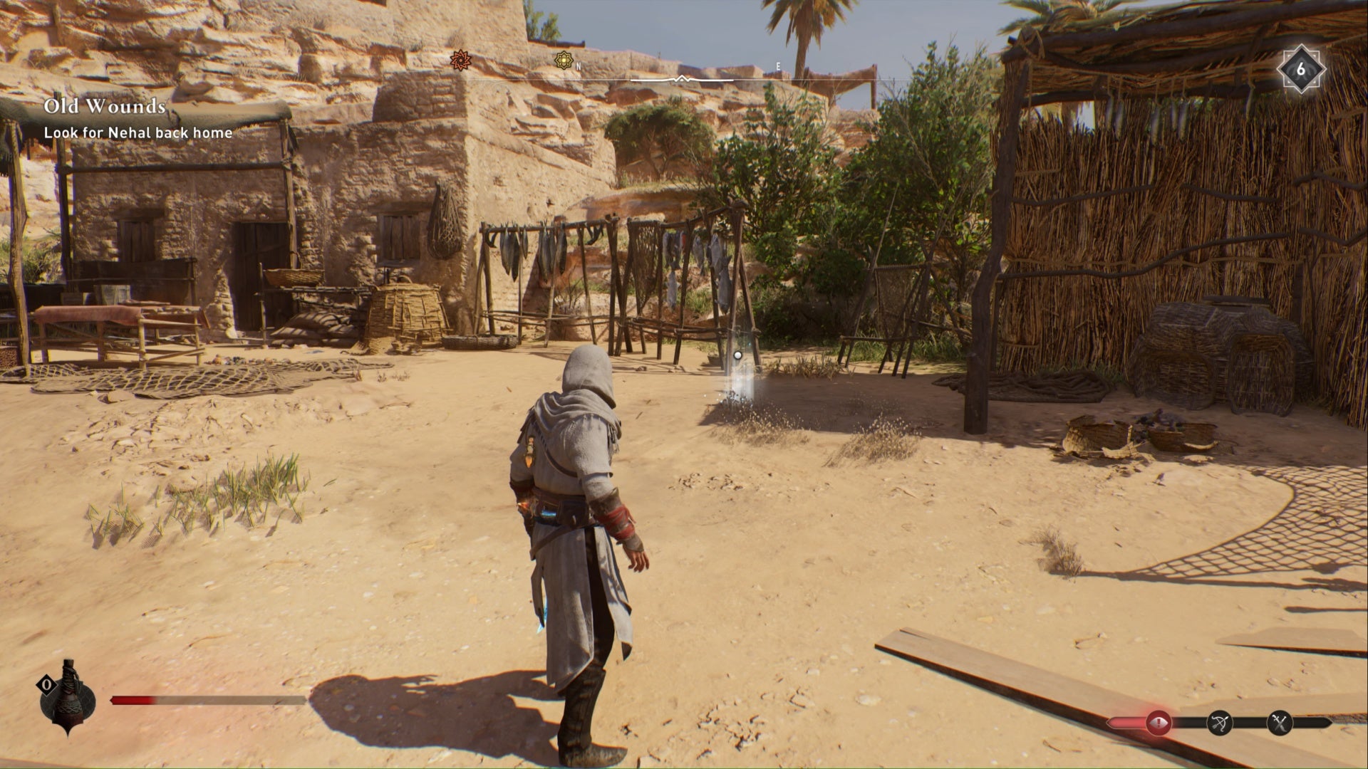 Assassins Creed Mirage, Basim se enfrenta al marcador brillante de la ubicación del tesoro enigma dejado atrás en una aldea abandonada.  A lo lejos se ven peces colgados de estructuras de madera, a la izquierda un edificio ya la derecha una cabaña adosada.