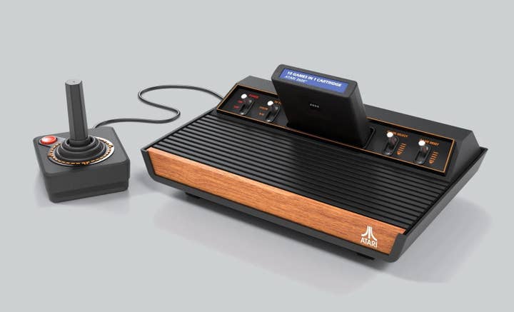 A picture of the Atari 2600+ console with a joystick attached and a 10-in-1 game cartridge plugged in. It has four-switches along the top edge of the console and a front plate with a wood-grain finish.