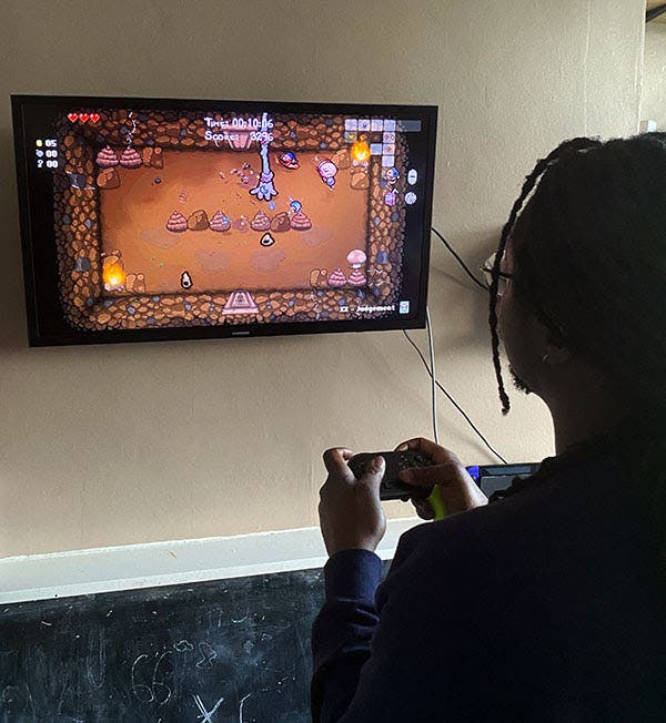 Larry Achiampong plays The Binding of Isaac on a wall-mounted television.