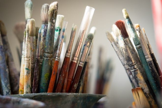 Photograph of paintbrushes with bits of paint on them standing upright in cups