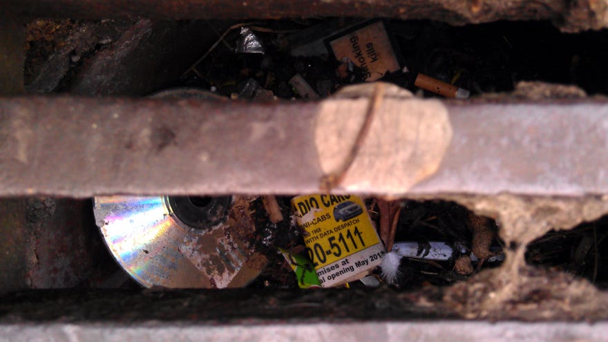 A CD seen beneath a drain gate in a photograph.