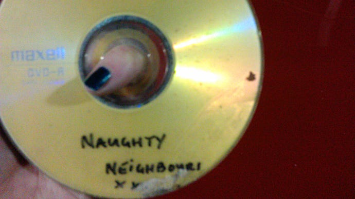 A photograph of a DVD-R with the half-scratched-off label "Naughty Neighbours XXX" written in pen.