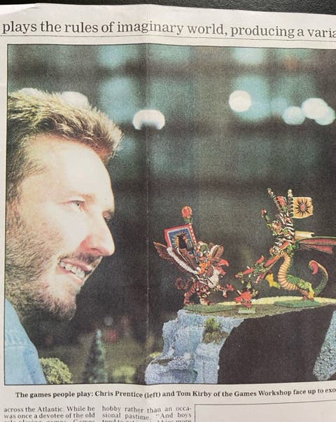 A newspaper clipping showing a photograph of a man gazing lovingly at two Warhammer fantasy figurines in battle. It's as if their god himself were looking down benevolently upon them.