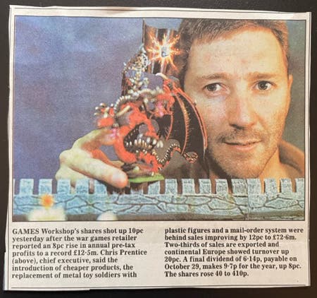 A newspaper clipping showing a photograph of a man of holding a Warhammer fantasy figurine up to the camera, as if it will produce some magical effect.