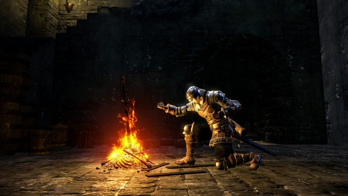 The player character in Dark Souls, a knight clad in armour, kneels before a bonfire