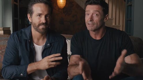 Ryan Reynolds and Hugh Jackman sitting side by side on a couch
