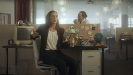 A still from Devolver Digital's E3 2021 showcase showing executive Nina Struthers sat on a chair in front of a desk while a man pinches food from her desk behind her.