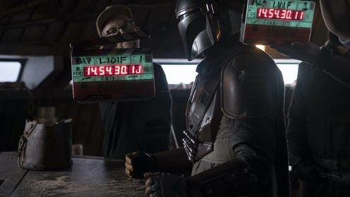 Set Still of The Mandalorian standing at a bar, directors are behind him holding clapperboards