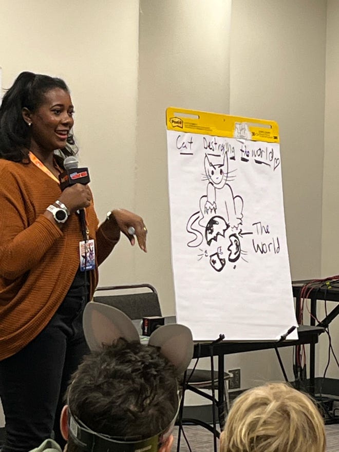 Liz Montague holding a microphone standing next to a large drawing pad