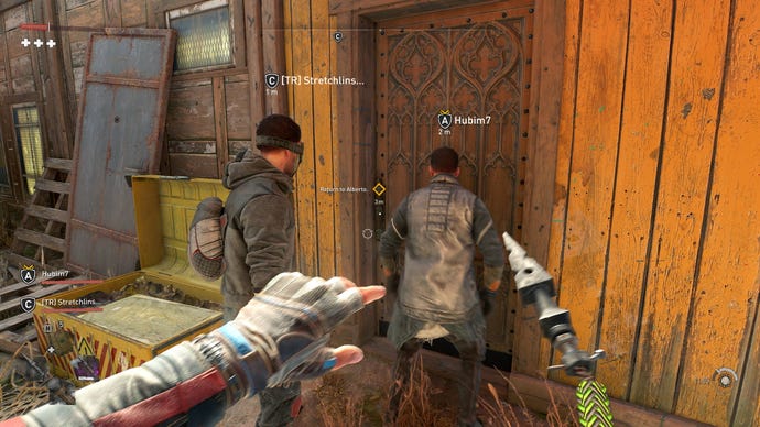The player stands behind two other humans, controlled by other players, as they enter a building in Dying Light 2's co-op mode
