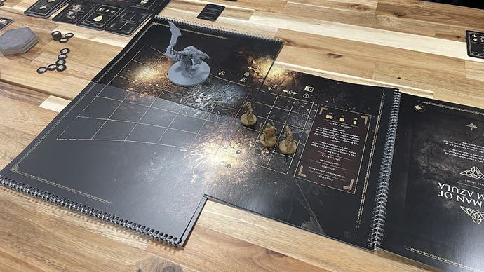 A wooden table with some black thick-paper game grids and pages laid out across it, and some little gold-coloured human figurines, and a big grey-coloured boss figurine. It's Elden Ring, the musical - sorry I mean board game.