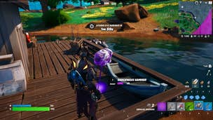 Fortnite Shockwave Hammer: An animated man in black pointy armor looks at a large purple hammer. Both are standing on a pier facing lush, green fields and large evergreen trees